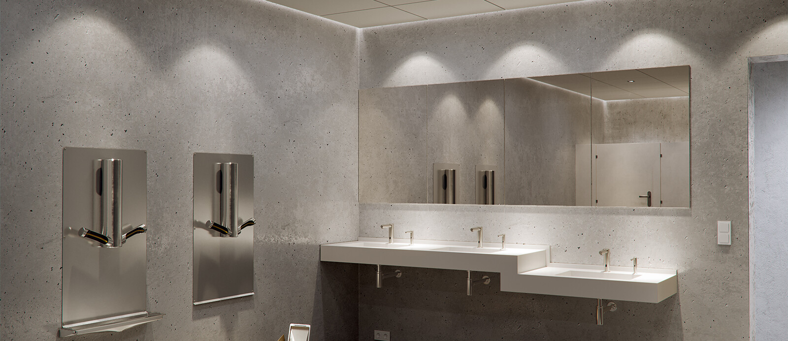 A bathroom made out of stone, with 2 Dyson Airblade Hand Dryers hanging on the wall next to each other and a drilling machine with some spare parts in a cardboard box standing in front of it on the ground.